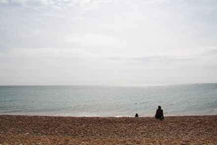 Tagesausflug nach Brighton, Am Strand mit Blick aufs Meer, vor dem Meer sitzen zwei Personen im Sand